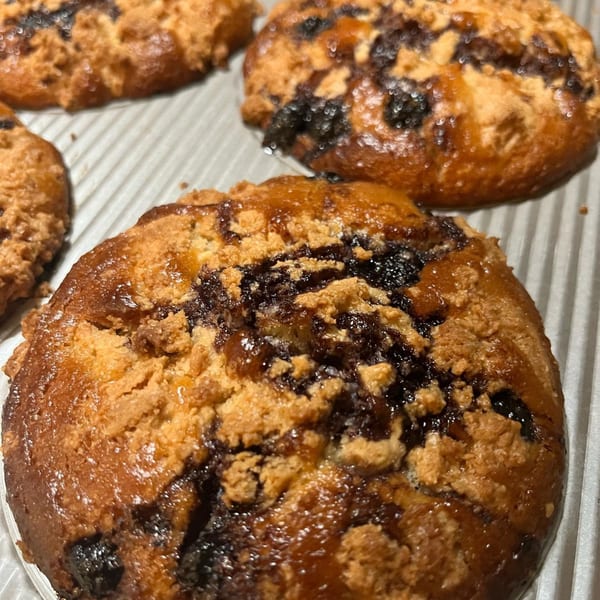Close-up of several blueberry crumb muffins with a shiny glaze on a baking sheet.