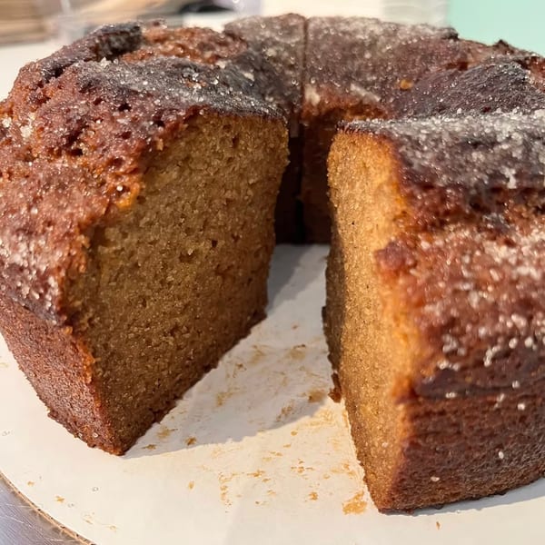 A round, golden-brown cake with a slice removed, topped with sparkling sugar.