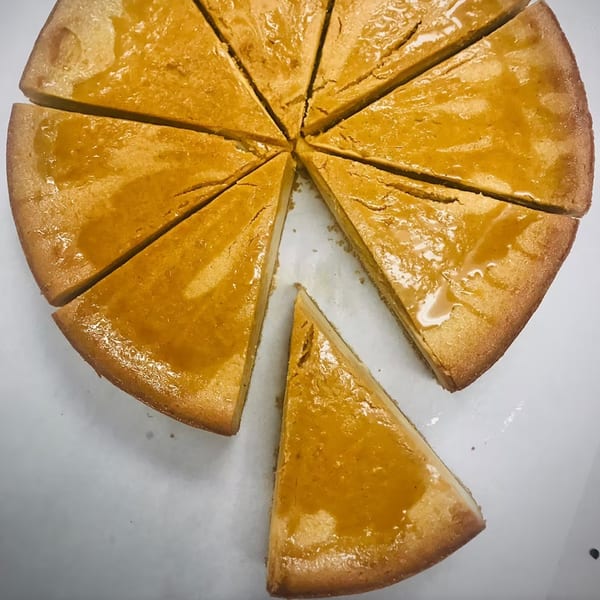A round, golden-brown How Delish HD cake, sliced into ten triangular pieces, with one piece separated.