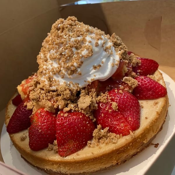 Cheesecake topped with fresh strawberries, whipped cream, and a crumble topping in a box.