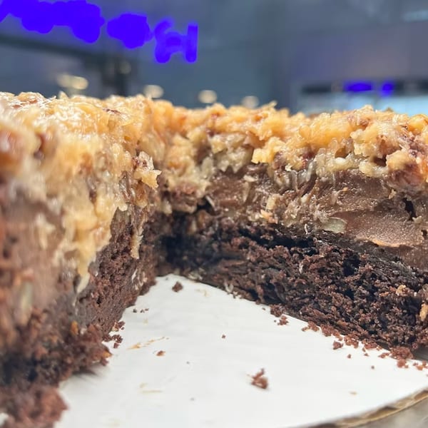A close-up of a German chocolate cake with a slice removed, showing rich layers of chocolate and coconut.