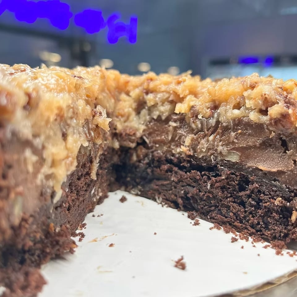 A close-up of a German chocolate cake with a slice removed, showing rich layers of chocolate and coconut.