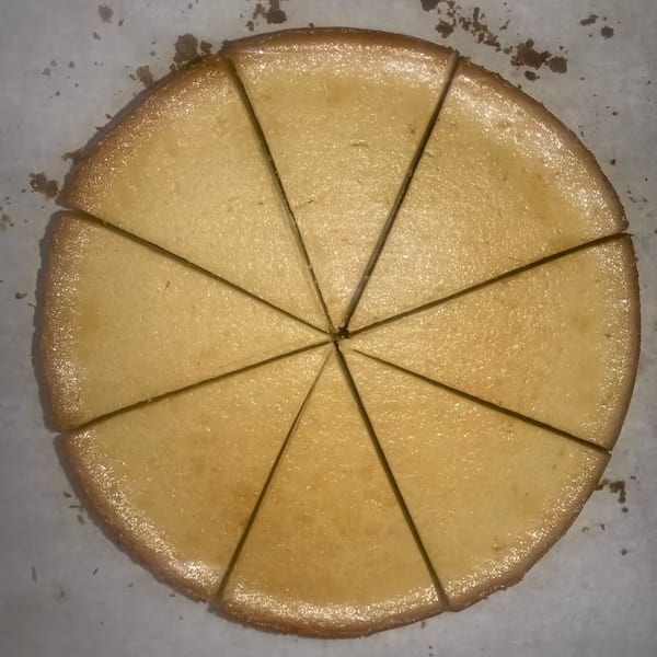 Overhead view of a round, golden-brown cake, sliced into ten triangular pieces on parchment paper.