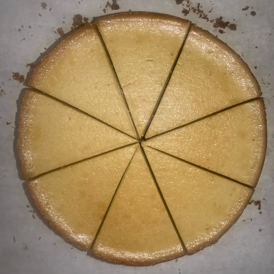 Overhead view of a round, golden-brown cake, sliced into ten triangular pieces on parchment paper.