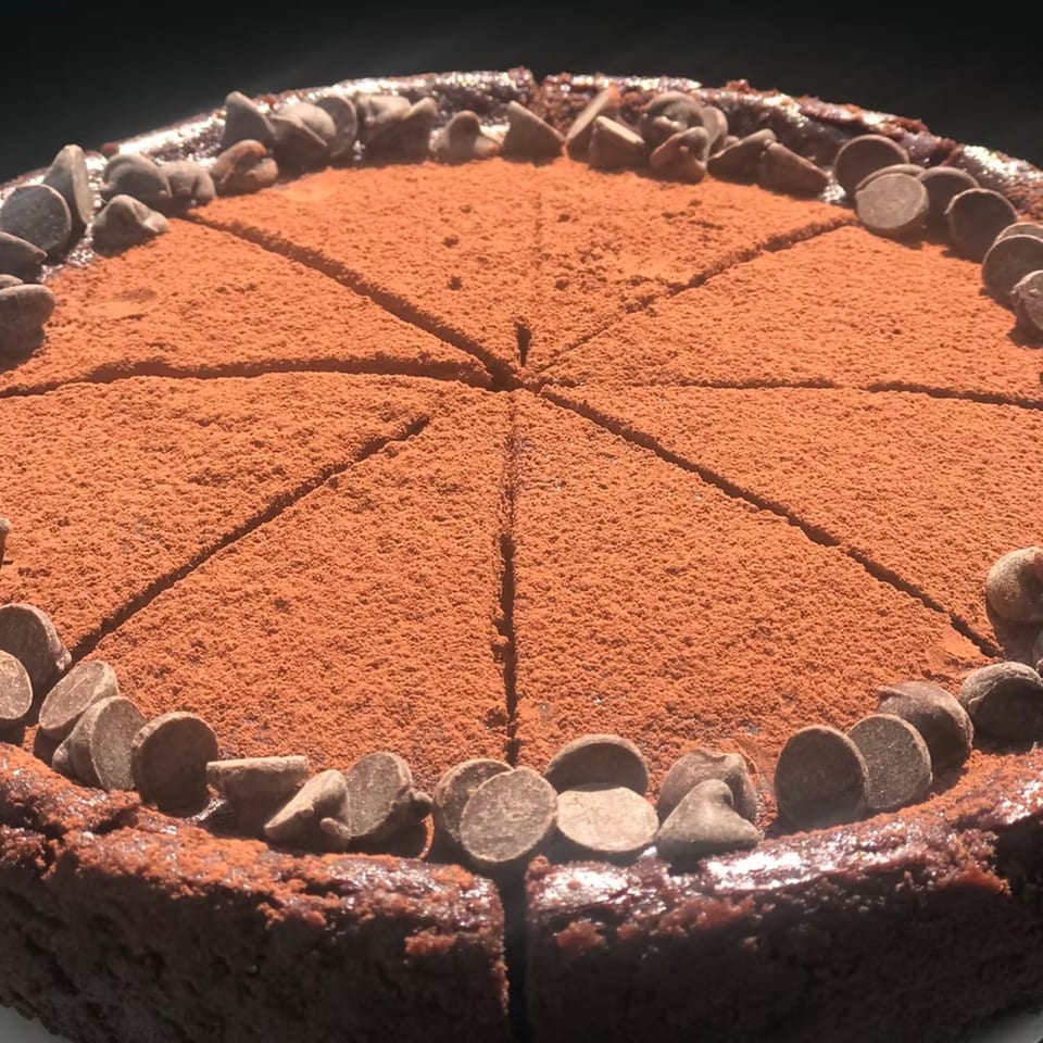 A chocolate cake from How Delish HD, dusted with cocoa powder and garnished with chocolate chips.