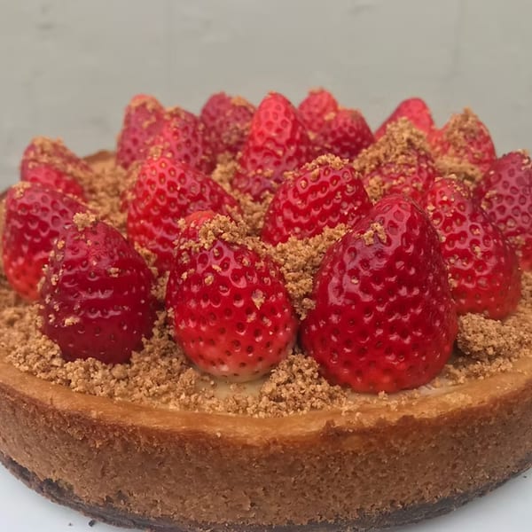 A cheesecake from How Delish HD topped with fresh strawberries and brown crumble.