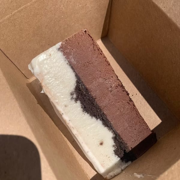 A rectangular dessert with layers of white, dark brown, and light brown, in a cardboard box.