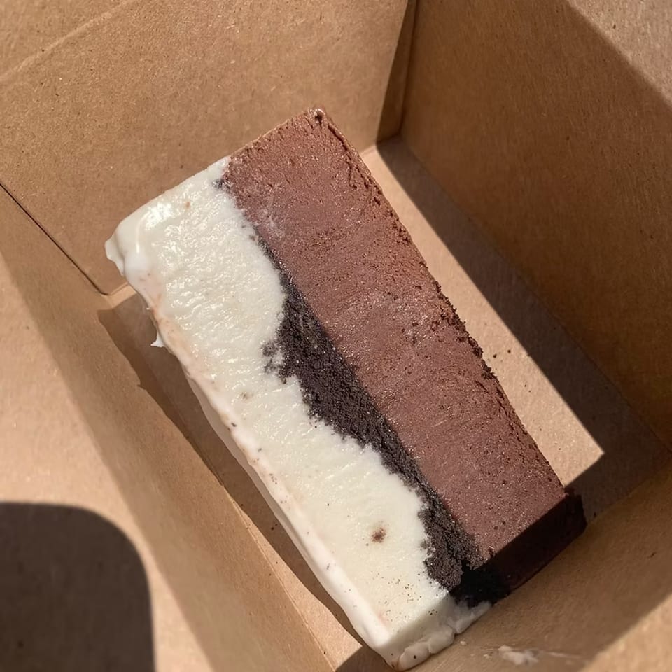 A rectangular dessert with layers of white, dark brown, and light brown, in a cardboard box.