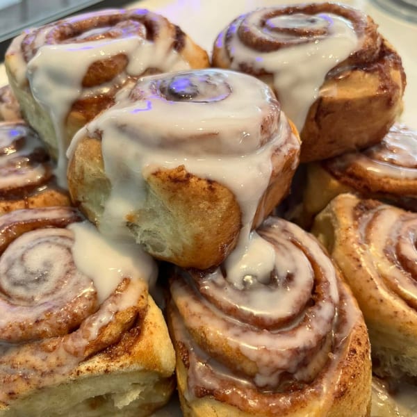A close-up of several cinnamon rolls generously topped with white icing, from How Delish HD.