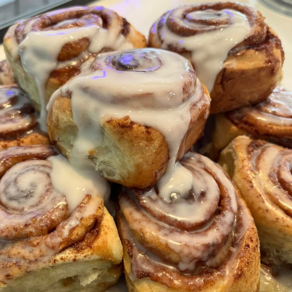 A close-up of several cinnamon rolls generously topped with white icing, from How Delish HD.