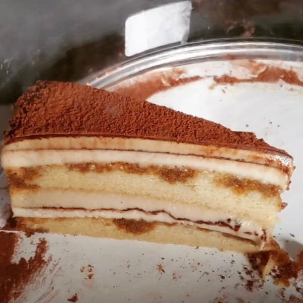 A slice of tiramisu with layers of cake, cream, and cocoa powder on a white plate.