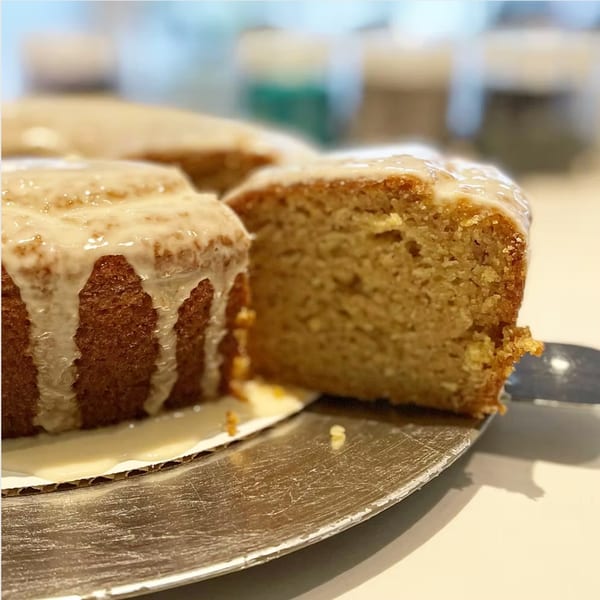 A slice of glazed cake on a silver server, with more cake in the background.