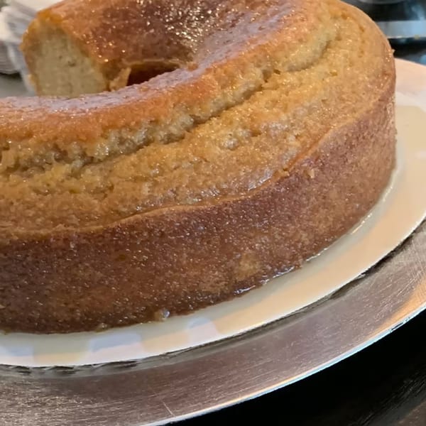 A golden-brown bundt cake with a glossy glaze sits on a white plate at How Delish HD.