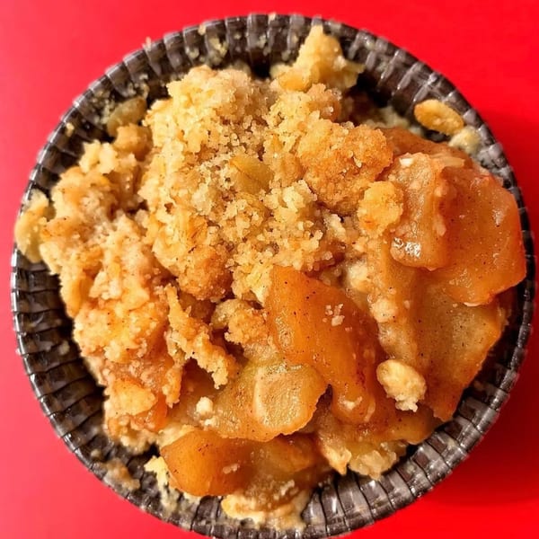 Close-up of a How Delish HD apple crumble dessert with a crumbly topping in a dark cup.