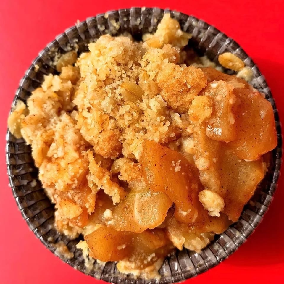 Close-up of a How Delish HD apple crumble dessert with a crumbly topping in a dark cup.