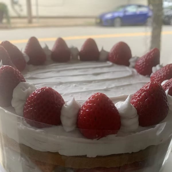 A strawberry shortcake with whipped cream and whole strawberries on top, seen through a window.